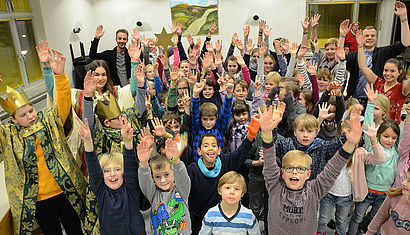 Sternsinger und Kinder freuen sich und recken die Arme in die Höhe..