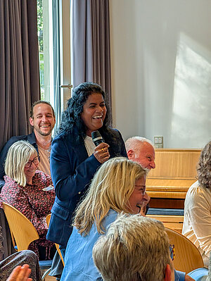 Menaka Kandeepan steht mit einem Mikrophon in der Hand bei der Jubiläumsveranstaltung im Haus der Familie Münster. 