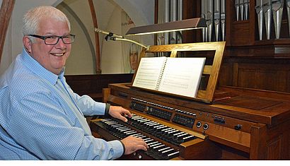 Norbert Cerfontaine sitzt an der Orgel der Nikolauskirche in Issum, seine Hände sind auf den Manualen, vor ihm ist ein Buch mit Noten aufgeklappt.