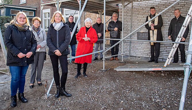 Mehrere Menschen stehen mit Abstand vor einem eingerüsteten Gebäude.