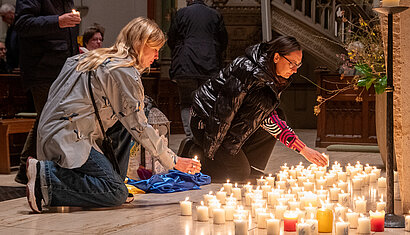 Zwei Frauen, die vor Kerzen auf dem Boden knien.