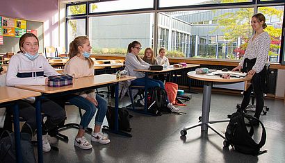 Fünf Mädchen sitzen in einem Klassenzimmer, auf der rechten Seite steht eine Lehrerin.