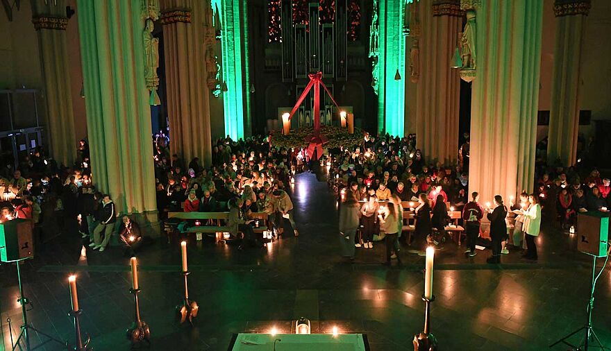 Blick von oben in eine Kirche, die nur wenig beleuchtet ist, einige Menschen halten Kerzen.