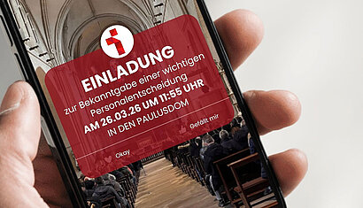 Auf einem Handybildschirm ist ein Bild des Doms mit folgendem Text zu sehen: Einladung zur Bekanntgabe einer wichtigen Personalentscheidung AM 26.03.26 UM 11:55 UHR IN DEN PAULUSDOM