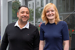 Ein Mann und eine Frau stehen nebeneinander vor einer Glastür und lächeln in die Kamera. Ein Mann und eine Frau stehen nebeneinander vor einer Glastür und lächeln in die Kamera.