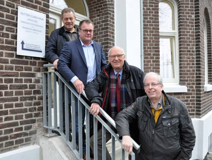 Vier Männer stehen auf einer Treppe, die nach links zum Eingang eines kernsanierten Hauses führt. Auf einem Schild links steht der Name Mutter-Clara-Haus.