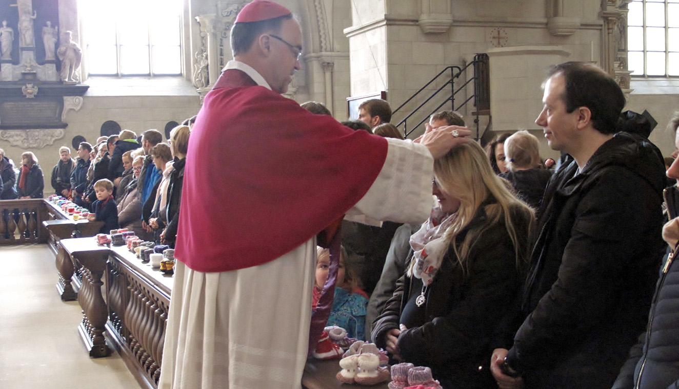 Weihbischof Rolf Lohmann segnet eine Frau, die ein Kind erwartet.