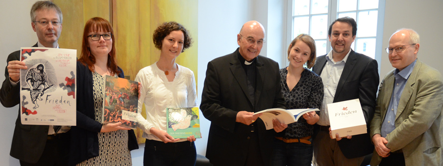 Bischof Felix Genn und Generalvikar Norbert Köster erhalten den Ausstellungskatalog, ein Kinderbuch und Plakate von drei Frauen und zwei Männern.