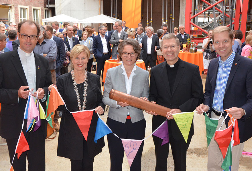 Pfarrdechant Markus Trautmann, Bürgermeisterin Lisa Stremlau, Ministerin Ina Scharrenbach, Weihbischof Dr. Stefan Zekorn und Landrat Dr. Christian Schulze Pellengahr halten Wimpel in der Hand.