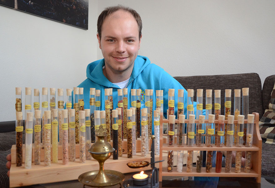 Benedikt Rottmann zeigt seine Weihrauchsammlung. Vor ihm stehen zahlreiche Reagenzgläser in einem Holzständer.