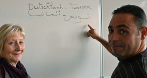 Marouan Gzara hat auf einer Tafel die Wort "Deutschland" und "Tunesien" in Deutsch und Arabisch geschrieben und erklärt sie Karin Badde-Struss.