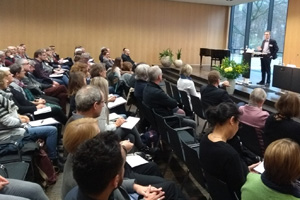 Das Publikum hört einem am Pult stehenden Referenten zu. Das Publikum hört einem am Pult stehenden Referenten zu.