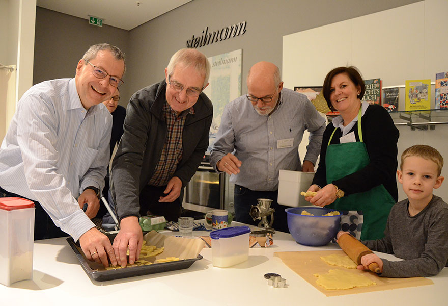 Fünf Personen stehen um den Tisch und stechen Plätzchen aus dem Teig aus.