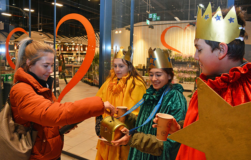 Sternsinger nehmen Spenden vor einem Supermarkt entgegen.