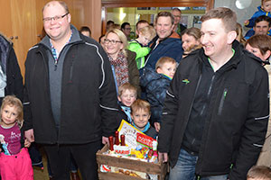 Zwei Männer tragen eine Kiste mit Süßigkeiten. Dahinter stehen viele Eltern und Kinder.