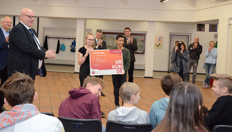 Die beiden Klassensprecher tragen ein großes Schild, während Hans-Georg Lambertz von der Bundeszentrale für politische Bildung ihnen gratuliert.