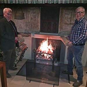 Zwei Männer stehen links und rechts vom Herdfeuer auf dem Bauernhof.