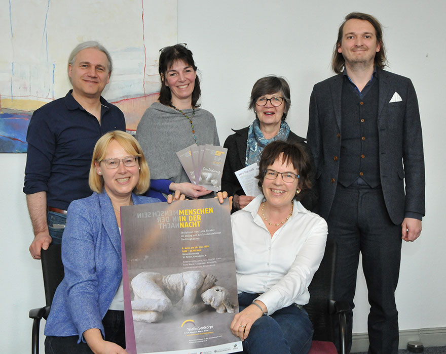 Die Verantwortlichen haben sich zum Gruppenbild aufgestellt und halten ein Plakat der Ausstellung in den Händen.