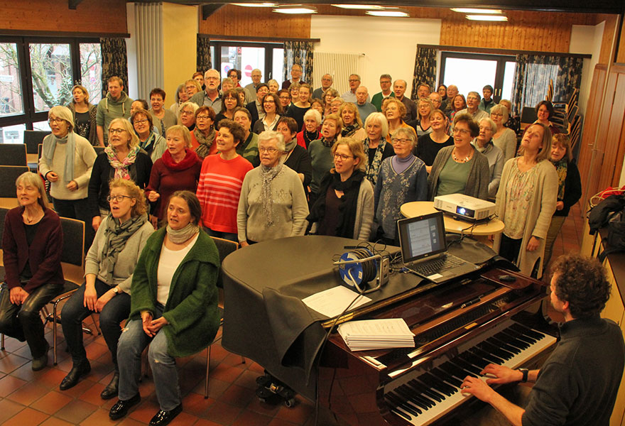 Im Vordergrund spielt Thorsten Maus am Klavier. Die Sängerinnen und Sänger sitzen im Saal. Im Vordergrund spielt Thorsten Maus am Klavier. Die Sängerinnen und Sänger sitzen im Saal.