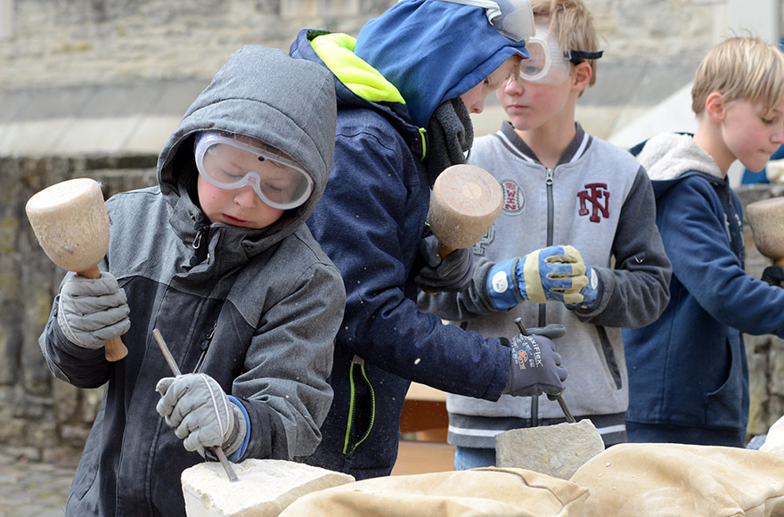 Kinder arbeiten mit Knüpfel am Steinblock. 