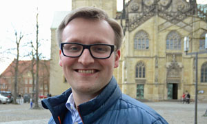 Jan Tasler steht lächelnd auf dem Domplatz in Münster.