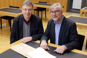 Dr. Peter Behrenberg, Leiter der Diözesanbibliothek (links) und Dr. Franz Josef Ratte sitzen an einem Tisch in der Bibliothek. Vor sich auf dem Tisch liegt ein aufgeschlagenes Schriftstück.