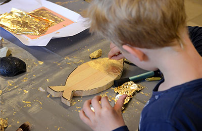 Ein Junge verziert einen Fisch aus Holz mit Gold.