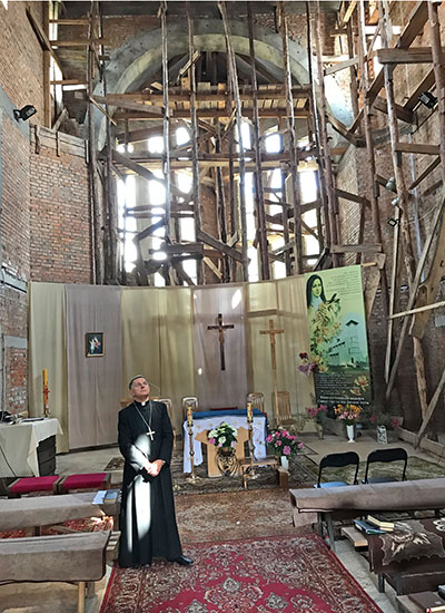 Ein ukrainischer Priester steht in einer Kirche, die mit einem Gerüst ausgebaut ist. In der Mitte ist ein kleiner Altar aufgebaut. 