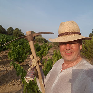 Johannes Arntz steht mit Spitzhacke und Sonnenhut im Weinberg.