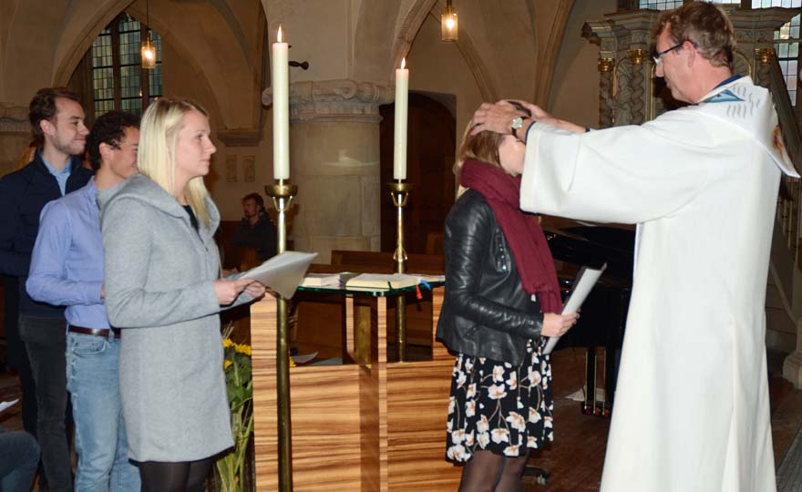 Pfarrer Thomas Laufmöller steht rechts im Bild und legt einer jungen Frau segnend die Hände auf den Kopf. Auf der linken Seite stehen drei weitere junge Leute an.