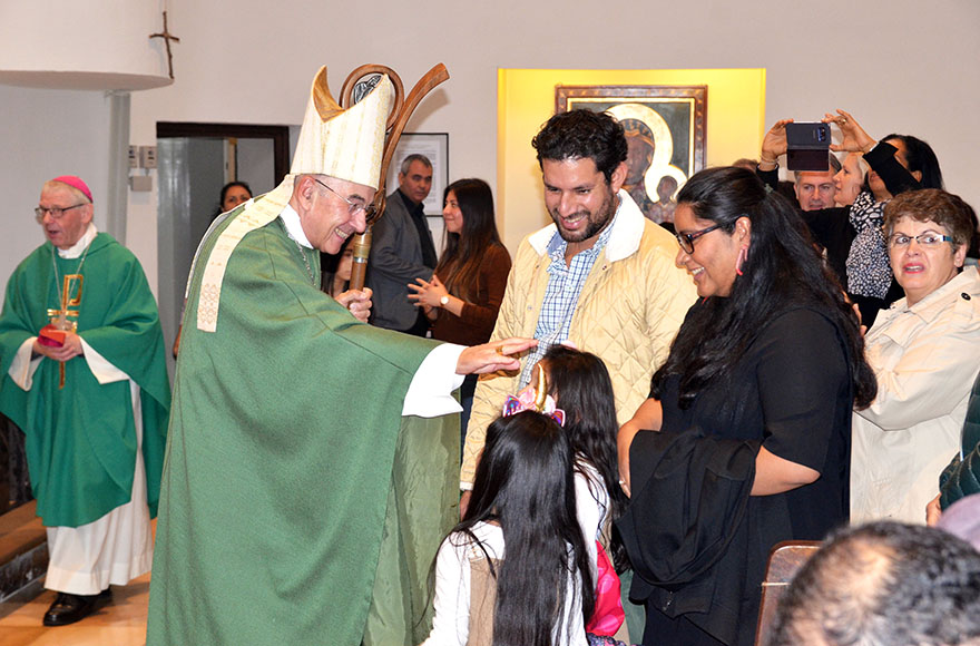 Der Bischof begrüßt eine spanischsprachige Familie in der Kirche.