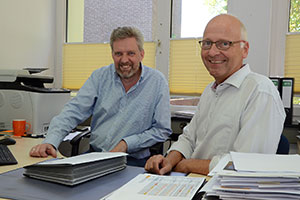 Josef Vossel und Norbert Mertens sitzen nebeneinander am Schreibtisch.