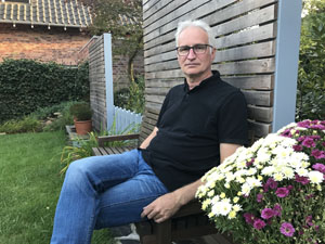 Martin Schmitz sitzt mit Jeans und Pullover bekleidet in einem Garten auf einer Bank
