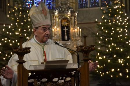 Bischof Genn am Ambo, im Hintergrund leuchten Kerzen an Weihnachtsbäumen, dazwischen der Hochaltar..