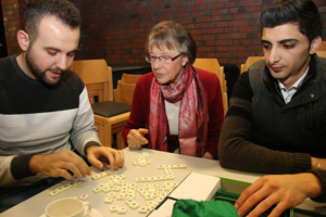 Eine Frau und zwei Männer legen Worte aus Scrabblesteinen auf einem Tisch.