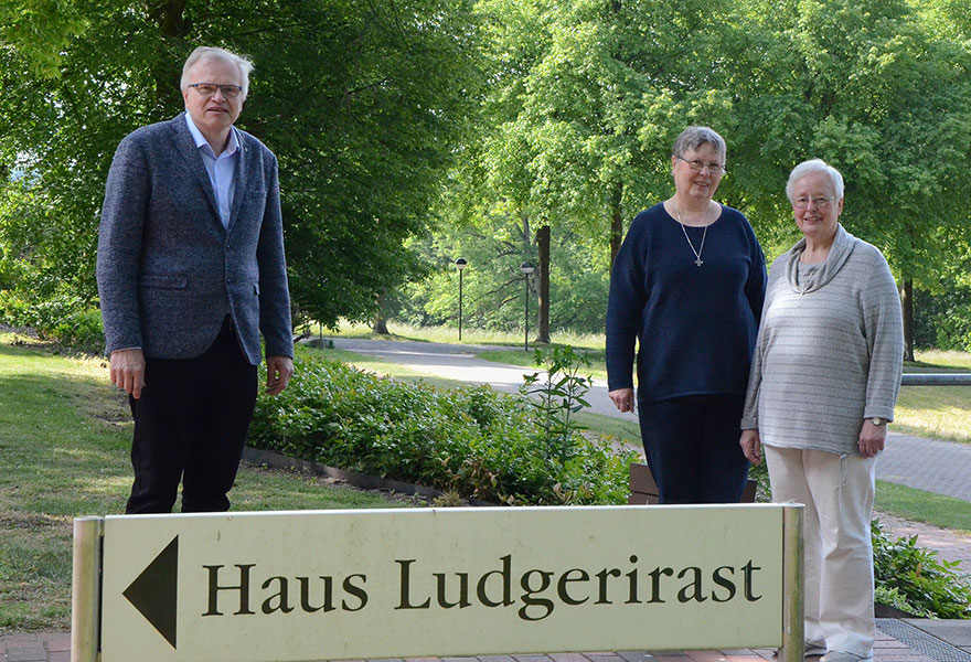 Andreas Geilmann, Schwester Mathilde Holstegge und Schwester Silvia Gossens (von links) stehen in Abstand zueinander. Davor ist ein Schild mit dem Titel "Haus Ludgerirast" zu sehen.