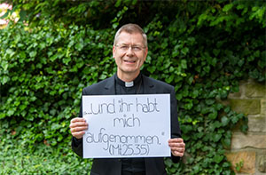 Weihbischof Stefan Zekorn hält ein Plakat mit der Aufschrift "... und ihr habt mich aufgenommen (Mt 25,35)" in den Händen. Weihbischof Stefan Zekorn hält ein Plakat mit der Aufschrift "... und ihr habt mich aufgenommen (Mt 25,35)" in den Händen.