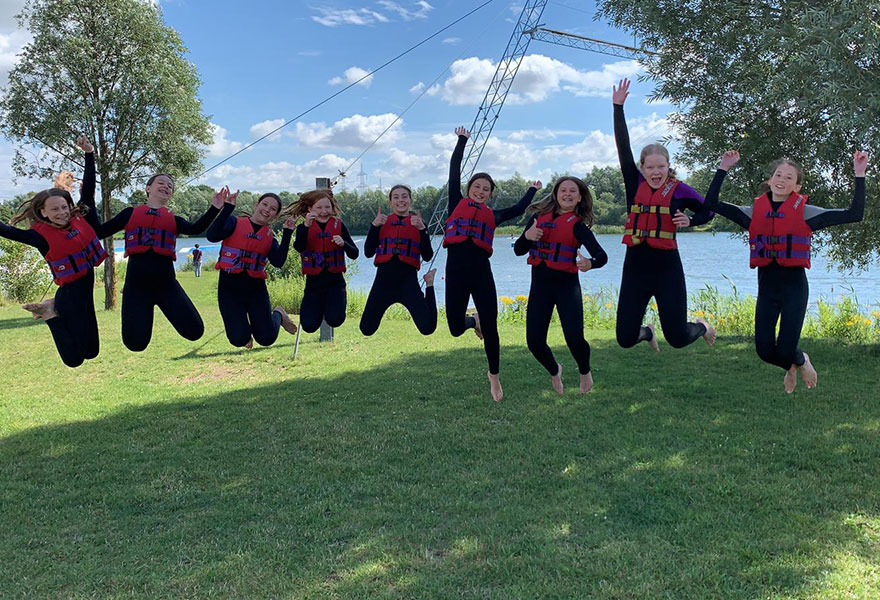 Neun Mädchen mit Rettungswesten springen vor Freude in die Luft.