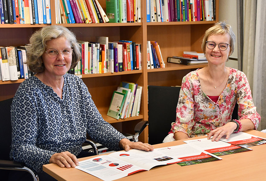 Ute Kieslich (links) und Beate Borgmann sitzen nebeneinander an einem tisch und lächeln in die Kamera.