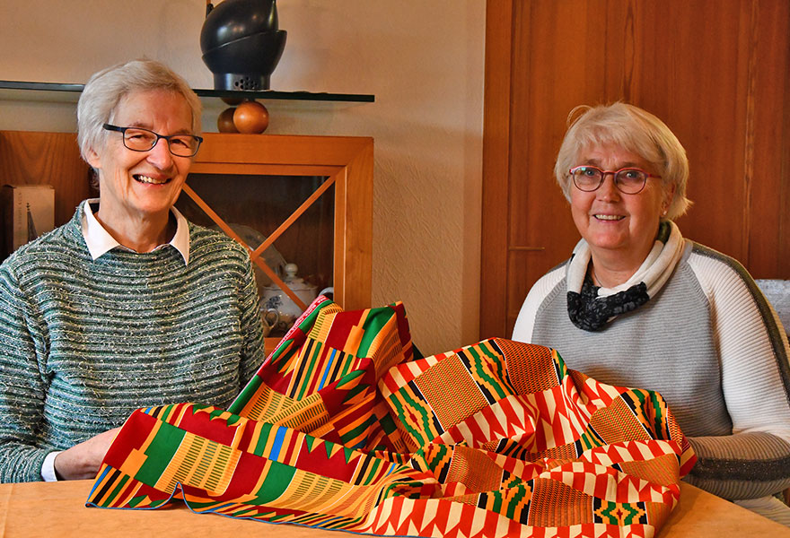 Mechthild Bäumer (links) und Anne David sitzen an einem Tisch und haben ein farbenfrohes Tuch aus Ghana in den Händen.