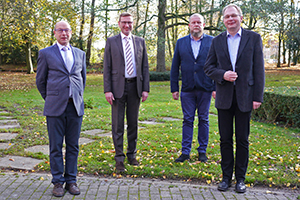 In blauen oder grauen Anzügen und hellen Oberhemden stehen die Mitglieder des Brüderrats nebeneinander, von links: Bruder Konrad Schneermann, Bruder Christoph von Netzer, Bruder Thomas Wierling und Bruder Karsten-Johannes Kruse. Im Hintergrund ist ein kleines Waldstück.