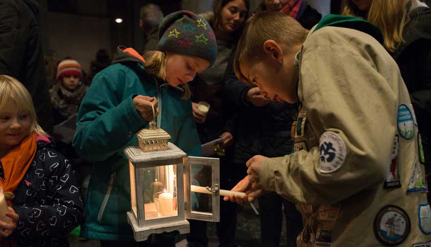 Ein Pfadfinder entzündet eine Kerze an der Laterne eines Mädchens.