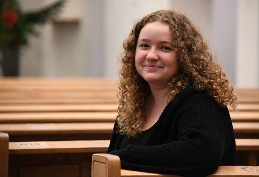 Jennifer Bergup sitzt in einer Kirchenbank und lächelt in die Kamera.