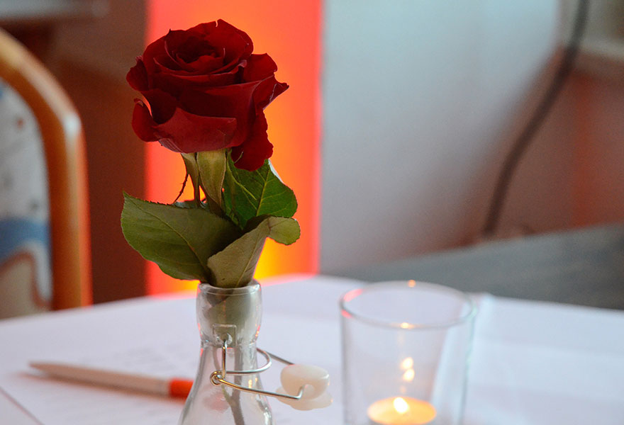Auf einem Tisch stehen eine rote Rose und eine Kerze.