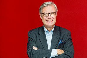 Porträt von Dr. Hermann Arnhold, der vor einer roten Wand steht.