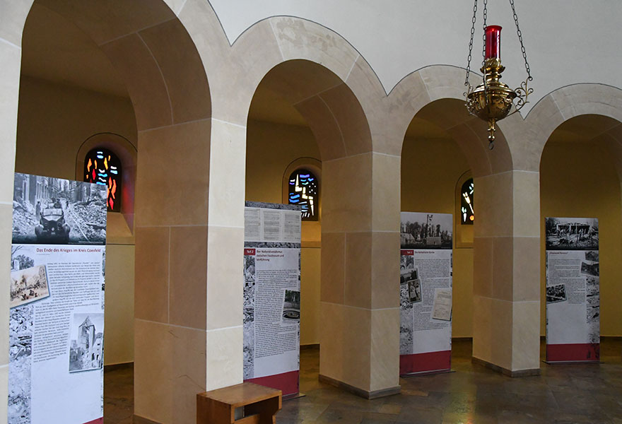 Zwischen den Rundbögen im Altarraum der Kirche stehen Banner mit Texten und Fotos.