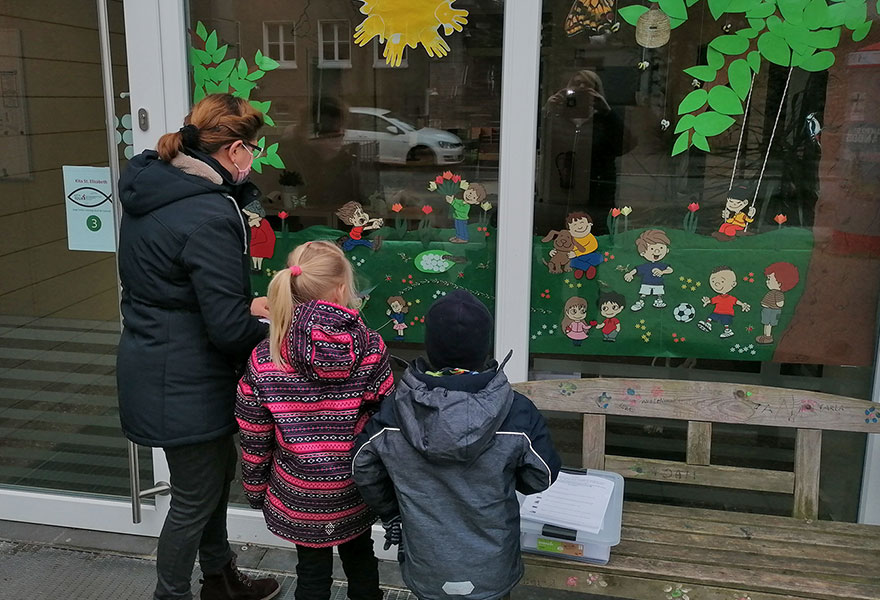 Eine Frau und zwei Kinder stehen vor einer Glasfront, die bunt gestaltet ist.