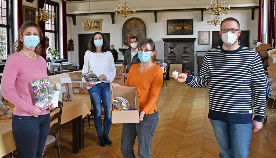 Mehrere Personen stehen in einem Saal und zeigen Andenken, die in ein Paket gefüllt werden.