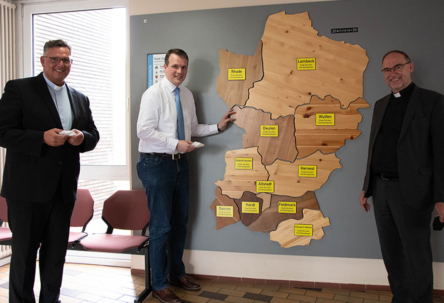 Pfarrer Dr. Stephan Rüdiger, Bürgermeister Tobias Stockhoff und Weihbischof Rolf Lohmann stehen an einer Karte aus Holz mit den verschiedenen Ortsteilen Dorstens.