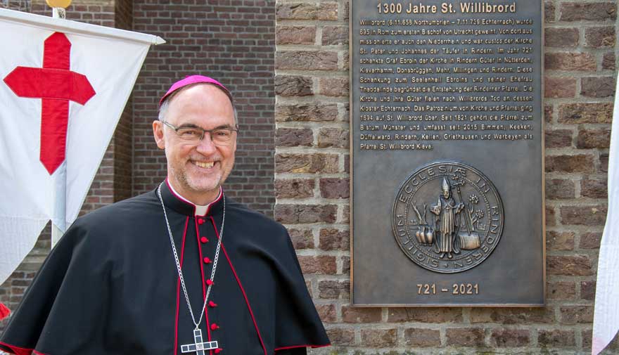 Weihbischof Rolf Lohmann steht neben der Bronzetafel in Rindern.